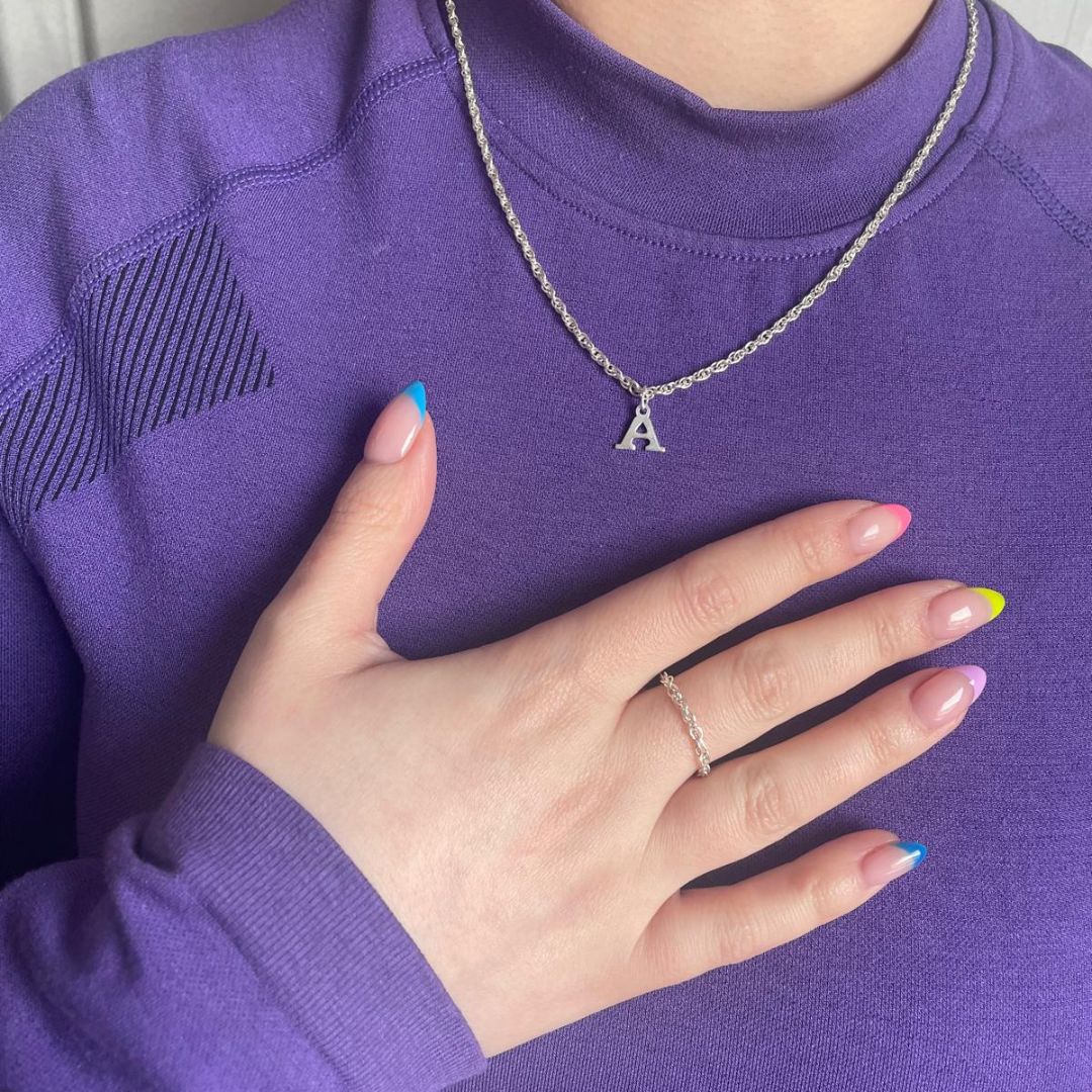A woman wearing a custom-fitted permanent necklace with an initial charm, placing her hand on her chest, showing the personalized design by Aura Eternity.