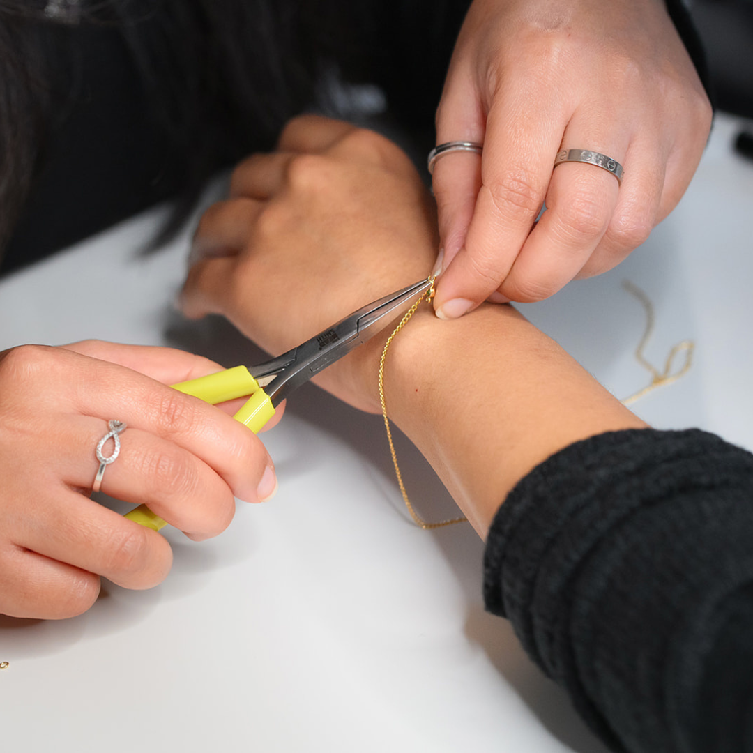 Hands working with pliers to adjust a gold bracelet on a wrist, showcasing the process of creating custom permanent jewellery and personalised permanent jewellery.