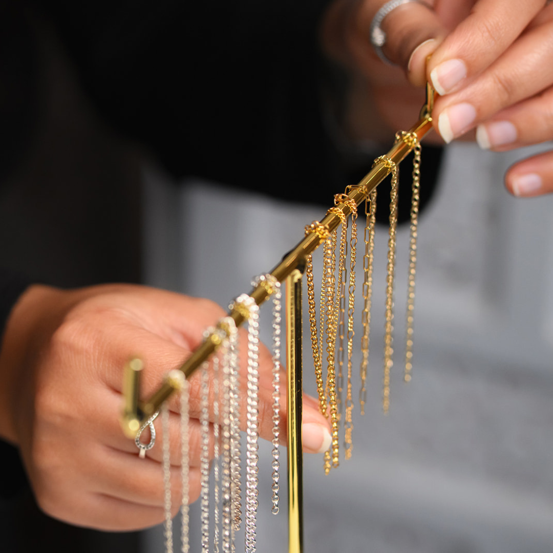 Hands holding a display rack with various styles of gold and silver permanent jewellery chains, showcasing luxury permanent jewellery, custom permanent jewellery styles, and personalised permanent jewellery from our Birmingham studio.