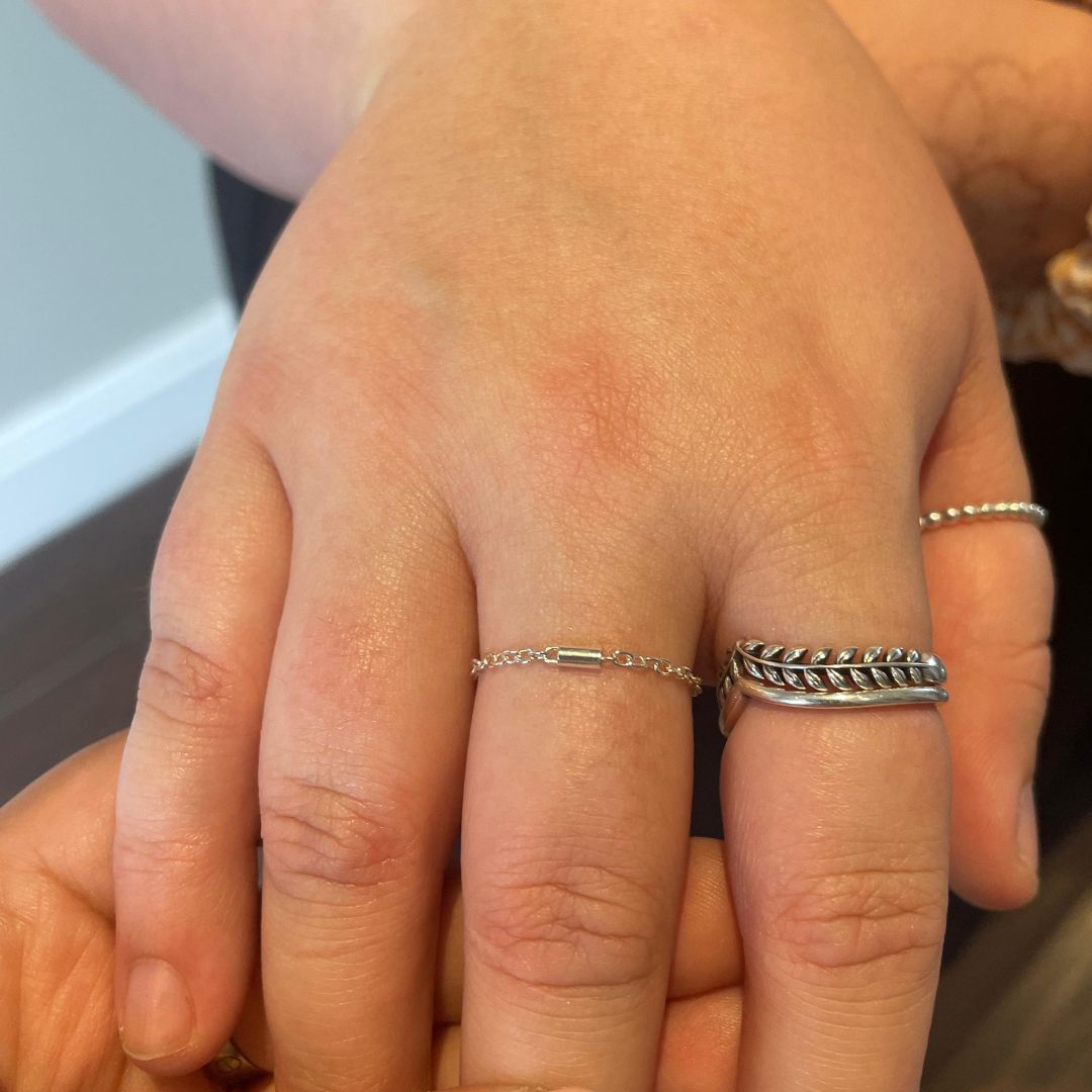 A hand displaying multiple custom-fitted permanent rings stacked together, showcasing a sleek and modern design by Aura Eternity.